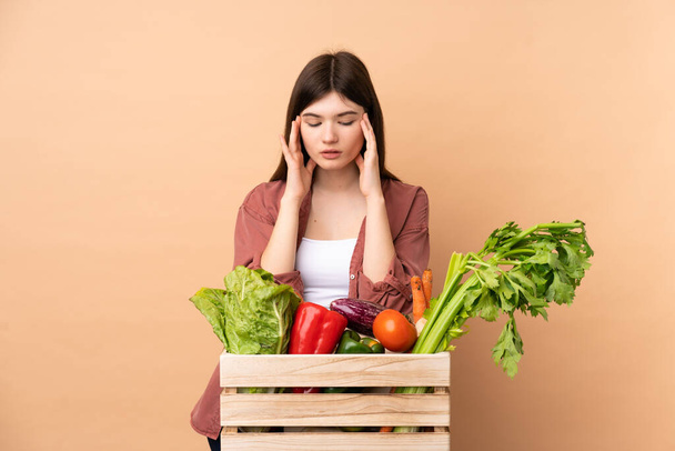 Jeune agricultrice avec des légumes fraîchement cueillis dans une boîte avec mal de tête - Photo, image
