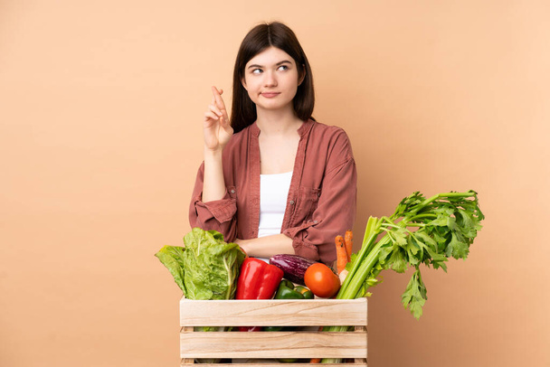 Młoda rolnik dziewczyna ze świeżo zebrane warzywa w pudełku z palcami skrzyżowania i życząc jak najlepiej - Zdjęcie, obraz