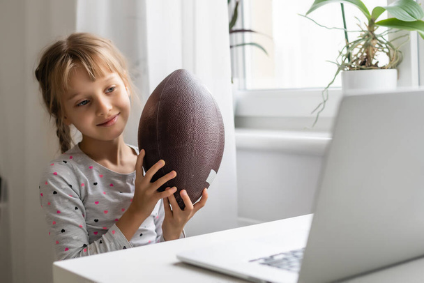 Internet addiction and computers concept with kid and laptop, little girl with rugby ball - Фото, зображення