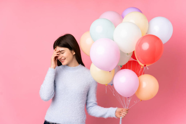 Young Ukrainian teenager girl holding lots of balloons over isolated pink background laughing - Photo, Image