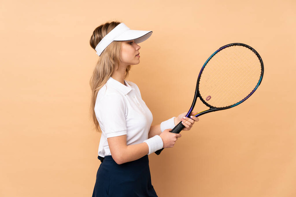 Неповнолітня російська дівчина, ізольована на бежевому фоні, грає в теніс. - Фото, зображення