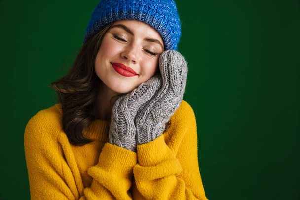 Beautiful happy girl in knit hat and mittens smiling at camera isolated over green background - Photo, image