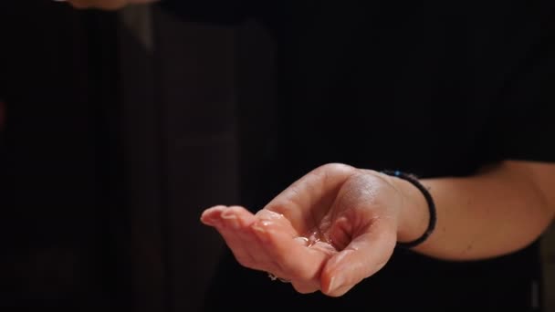 Masajista manos verter aceite de masaje en la mano femenina preparándose para relajar o revitalizar el procedimiento de masaje en el salón de belleza corporal spa. Fondo negro. 4 k vídeo - Metraje, vídeo