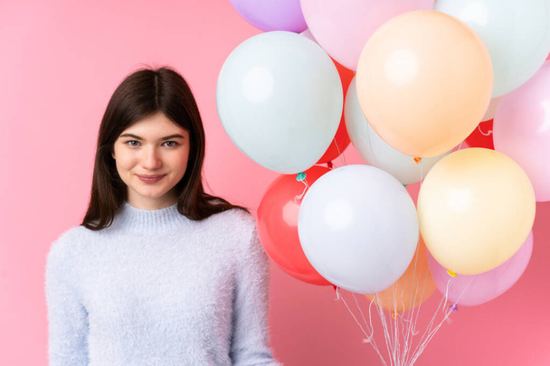 Junge ukrainische Teenager Mädchen hält viele Luftballons über isolierten rosa Hintergrund - Foto, Bild
