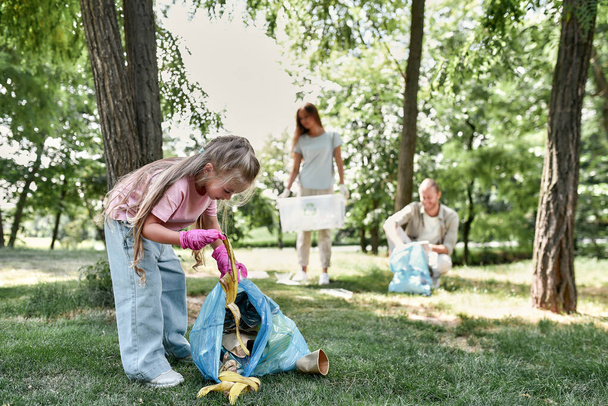 Linda niña con bolsa de basura recogiendo basura mientras limpia con los padres en el parque o el bosque - Foto, imagen