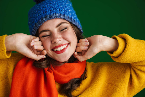 Cheerful beautiful young woman in sweater and hat standing isolated over green background - Φωτογραφία, εικόνα