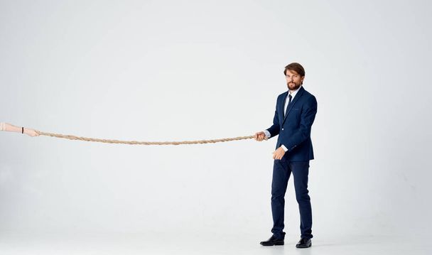 zakenman in een pak trekt een touw op een lichte achtergrond - Foto, afbeelding