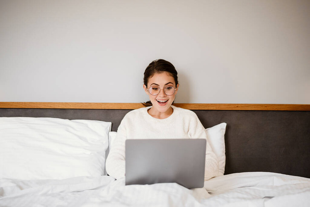 Beautiful cheerful girl smiling and using laptop while sitting in bad at home - Foto, immagini