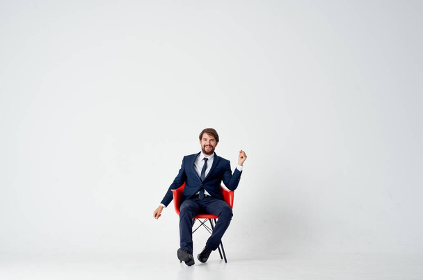 business man sits on red chairs indoors and gestures with his hands on a light background - Photo, Image