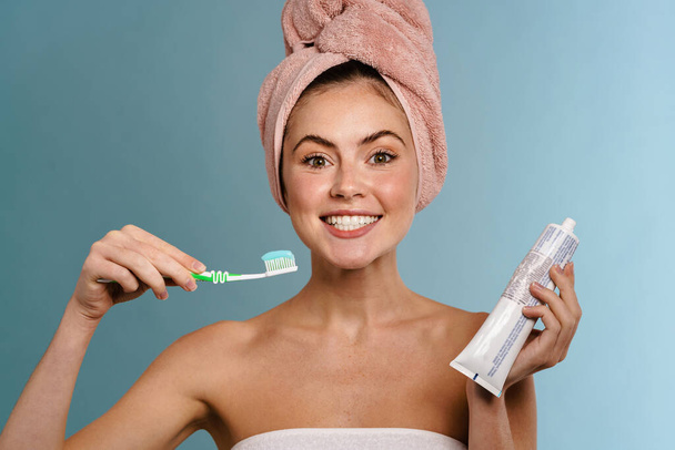 Nice excited girl wearing towels posing with toothpaste and toothbrush isolated over blue background - Foto, Bild