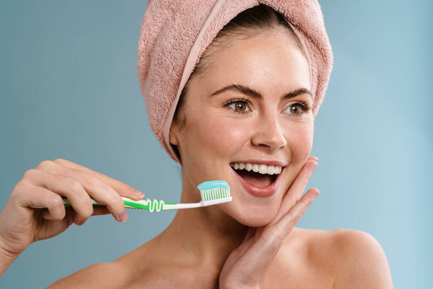 Image of a young happy positive woman in towel brushing her teeth isolated over blue wall background - Photo, image