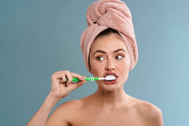 Image of a young beautiful woman in towel brushing her teeth isolated over blue wall background - Fotoğraf, Görsel