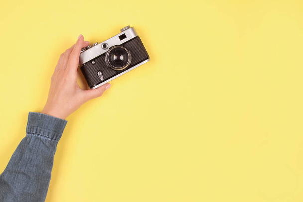 Skład w kolorach szarym i żółtym, kolor roku 2021 - kobieca ręka trzymająca stary aparat fotograficzny retro na żółtym tle z przestrzenią do kopiowania. Koncepcja szkoły fotografii online, selektywne ukierunkowanie - Zdjęcie, obraz