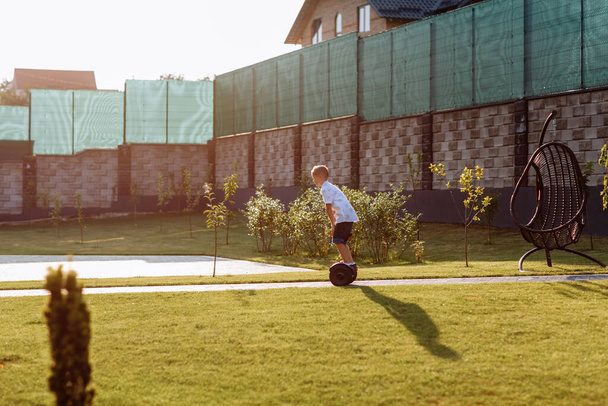 Modischer Teenager fährt auf einem Segway im Hof. Mode für Gyroscooter und Gyroboards bei Jugendlichen. Aktive Freizeitgestaltung der Kinder im Sommer. Intelligenter Ökotransport. - Foto, Bild