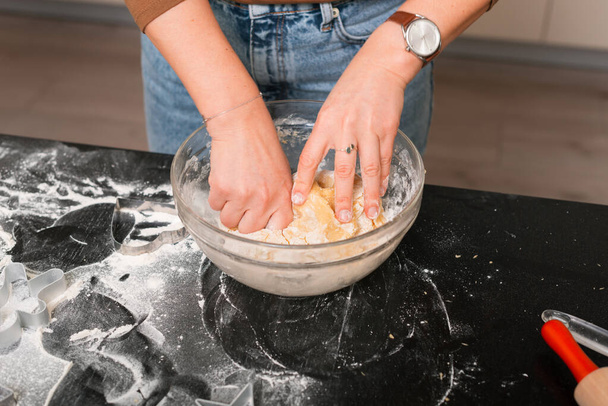 Les mains féminines pétrissent de la pâte sur une table noire. - Photo, image