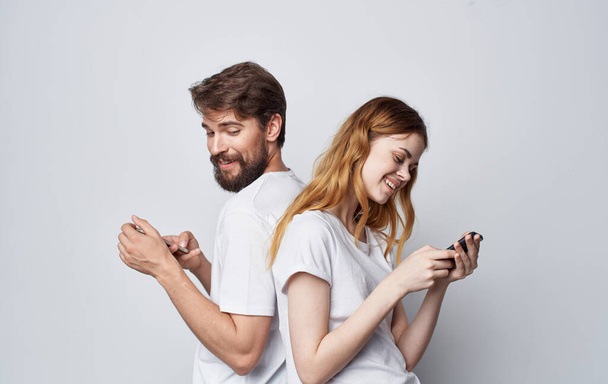 jong paar in witte t-shirts met telefoons in hun handen communicatie internet levensstijl - Foto, afbeelding