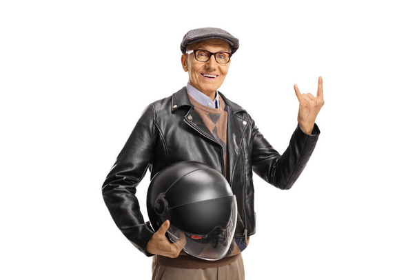 Elderly man in a leather jacket holding a helmet and gesturing a rock and roll sign isolated on white background - Photo, image