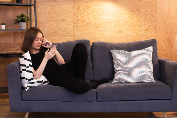 Молодая счастливая девушка лежит на диване с телефоном. - Фото, изображение