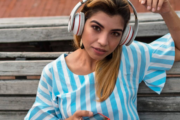Жінка слухає музику зі смартфона з гарнітурою в міському парку
 - Фото, зображення
