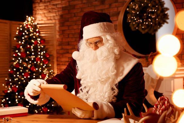 Santa Claus reading wish list at table indoors - Fotografie, Obrázek