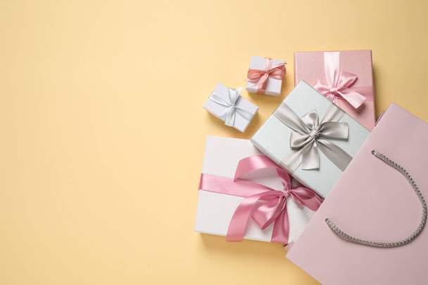 Sacchetto di carta con belle scatole regalo su sfondo beige, posa piatta. Spazio per testo - Foto, immagini
