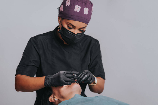 Giovane donna caucasica bionda che apre la bocca mentre il dentista etnico afroamericano in guanti di lattice bianchi controlla le condizioni dei suoi denti si concentra sul dentista - Foto, immagini