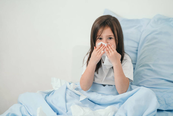 La niña se resfrió. Los niños estornudan en un pañuelo. El niño está enfermo y está siendo tratado en casa. Resfriados estacionales en niños - Foto, Imagen