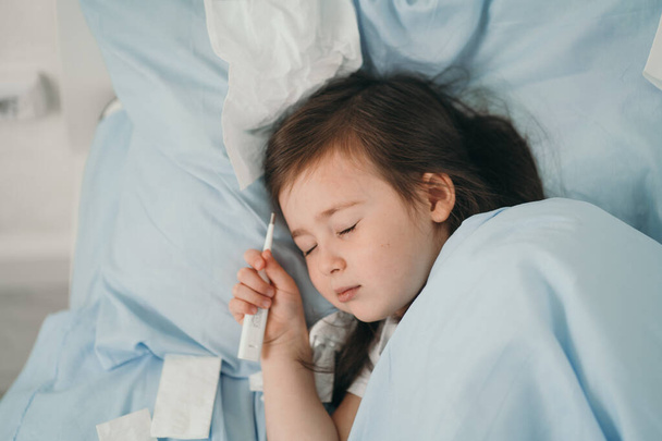 The little girl caught a cold. Children sneeze into a handkerchief. The child is ill and is being treated at home. Seasonal colds in children - Zdjęcie, obraz