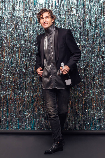 Holidays concept - happy tipsy man with bottle of champagne and wine glass at christmas or new year party on a sparkle background. - Zdjęcie, obraz