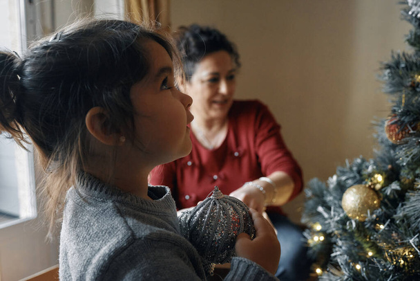 Großeltern schmücken mit ihrer kleinen Enkelin den Weihnachtsbaum - Foto, Bild