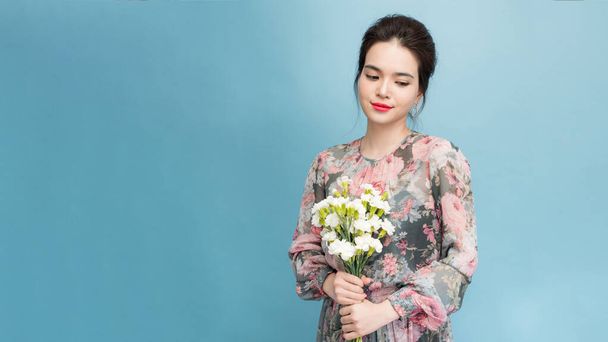 Headshot of pretty young woman with tender smile, healthy skin, carries bouquet of spring flowers, isolated over light blue background - Photo, image
