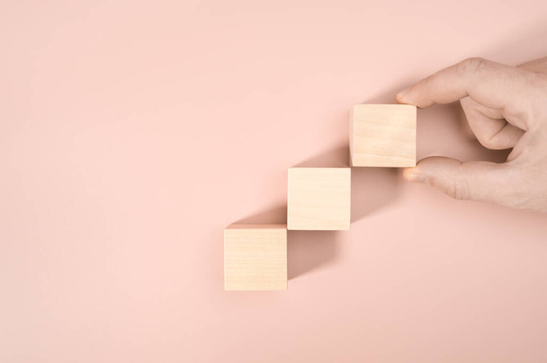 Business concept growth success process, Close up man hand arranging wood block stacking as step stair on pink background, copy space. - 写真・画像