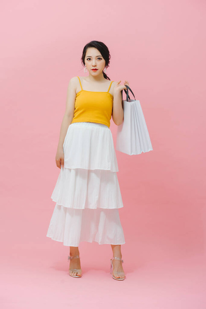 Shopping concept: vrolijke glimlachende modieuze vrouw in trendy kleding poserend met witte papieren tassen - Foto, afbeelding