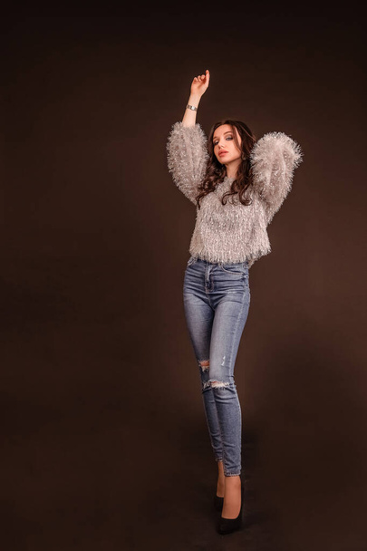 portrait beautiful girl poses on a black gray background. lady in jeans and grey fluffy sweater - Zdjęcie, obraz