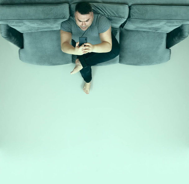middle aged man looking at screen of mobile phone, smartphone and relax on sofa.  - Foto, Imagen