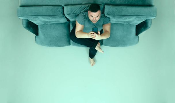middle aged man looking at screen of mobile phone, smartphone and relax on sofa.  - Foto, afbeelding