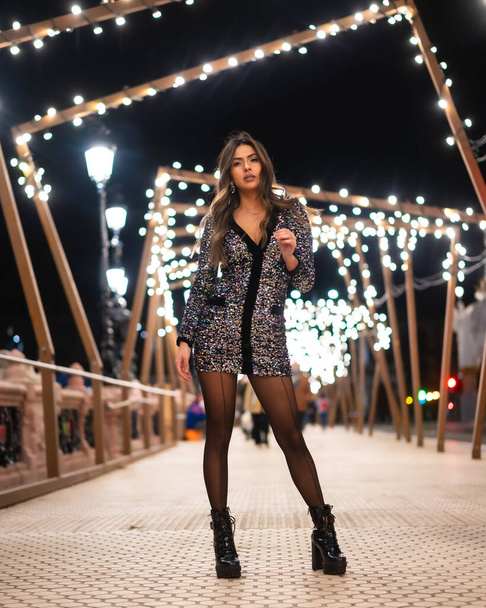 Christmas lifestyle. Young girl in a fashionable dress with sequins in the city christmas lights - Photo, Image