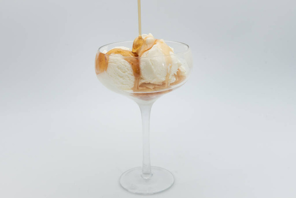 Vanilla ice cream with spilling caramel syrup in glass on white background. - Foto, Imagem