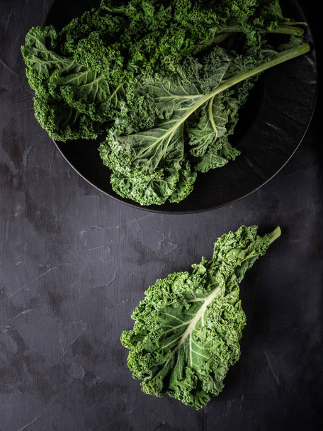 Fresh green kale leaves on dark table. Overhead shot with copy space. - Photo, Image
