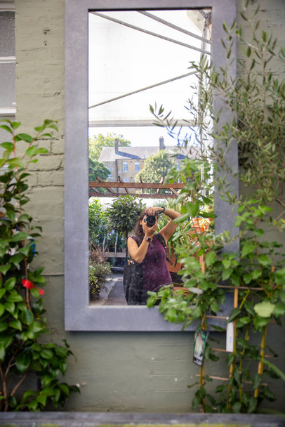Jonge vrouw neemt een zelfportret in een raam omringd door planten - Foto, afbeelding