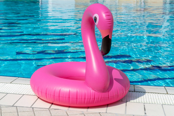 Letnia zabawa odizolowana. Różowy dmuchany flaming w wodzie basenowej na letnie tło plaży. Zabawna zabawka dla dzieci - Zdjęcie, obraz