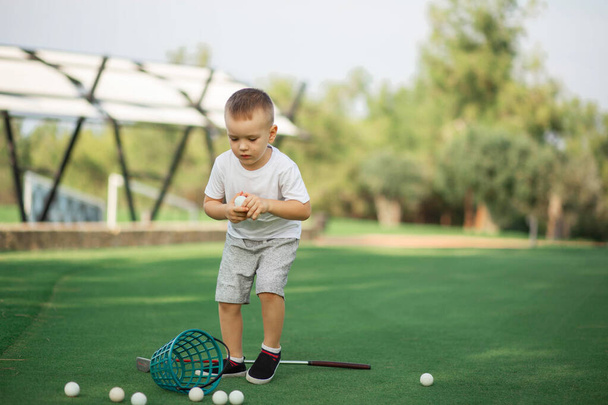 Mały chłopiec golfista ze swoim plastikowym zestawem golfowym na zielonym polu, zbierając swoje piłki golfowe w koszykówce - Zdjęcie, obraz