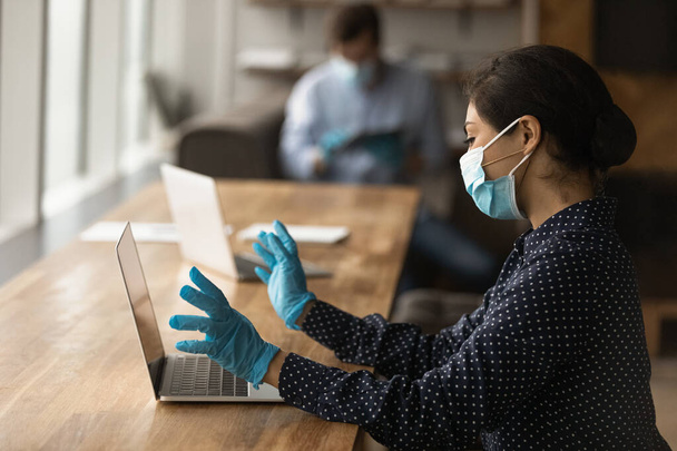 Female worker in medical facemask work on laptop - Foto, afbeelding