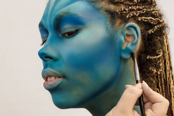 Artista de maquillaje aplica ye sombras a una hermosa mujer en estilo Avatar - Foto, Imagen