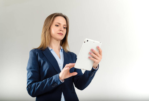 Jonge zakenvrouw maakt gebruik van tablet geïsoleerd op grijze achtergrond - Foto, afbeelding