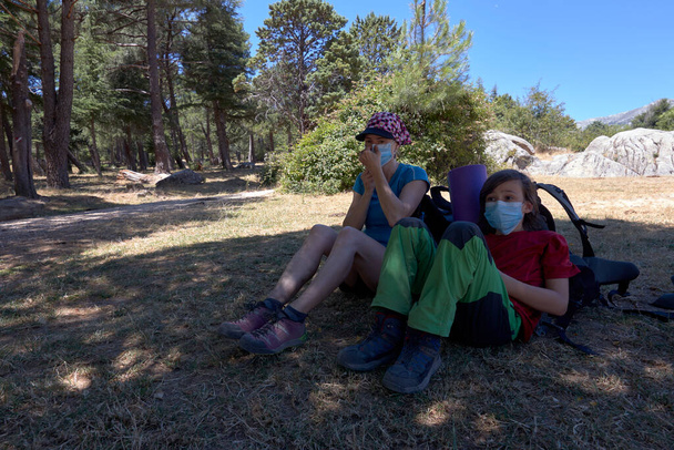 Famille de deux personnes se relaxant dans une forêt en randonnée, ils portent le masque médical. - Photo, image