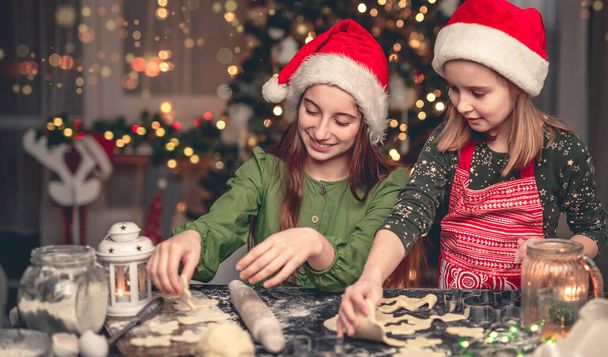 Happy sisters making cookies under christmas tree - Foto, Imagen
