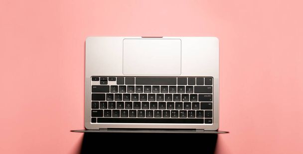 Layout minimalista girato con un moderno computer portatile grigio argento con una tastiera nera su uno sfondo rosa colorato. - Foto, immagini