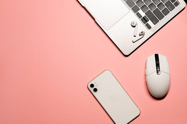 Minimal flat lay foto con un computer portatile grigio argento, smartphone moderno, mouse in plastica bianca, e auricolari wireless su uno sfondo rosa pastello. - Foto, immagini