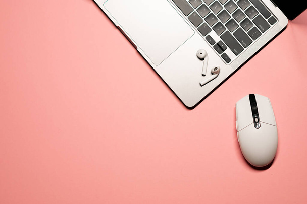 Minimaliste plat poser photo sur un fond rose pastel avec un ordinateur portable gris argenté moderne, écouteurs sans fil, et une souris d'ordinateur en plastique blanc. - Photo, image
